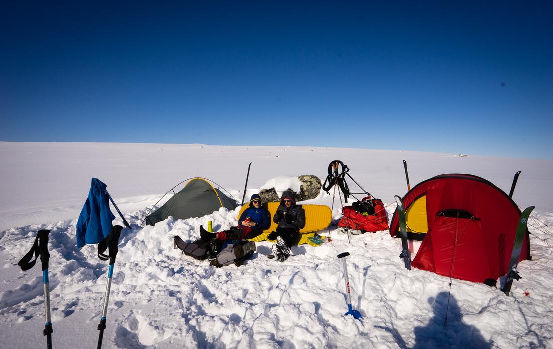 Group sitting in the snow surrounded by tents during a winter wilderness expedition.
