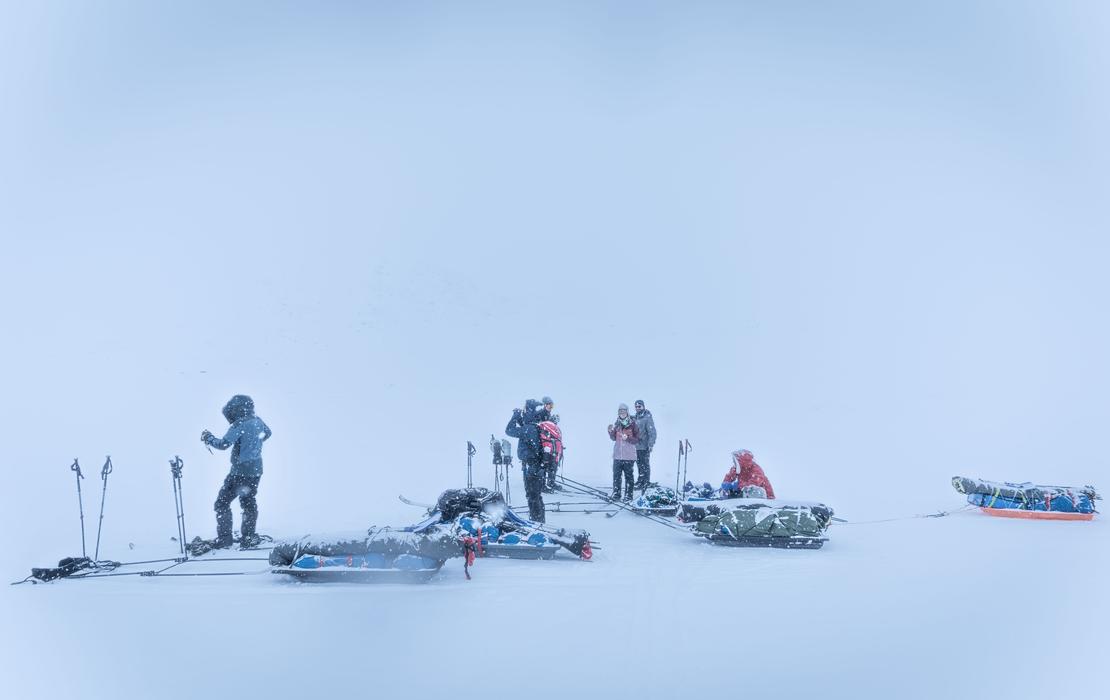 Skiers moving through thick fog in a snowy, featureless Arctic landscape.