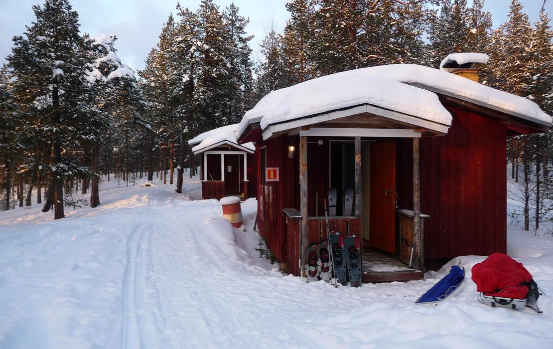 Row of cozy wooden cabins in a snowy Lapland landscape.
