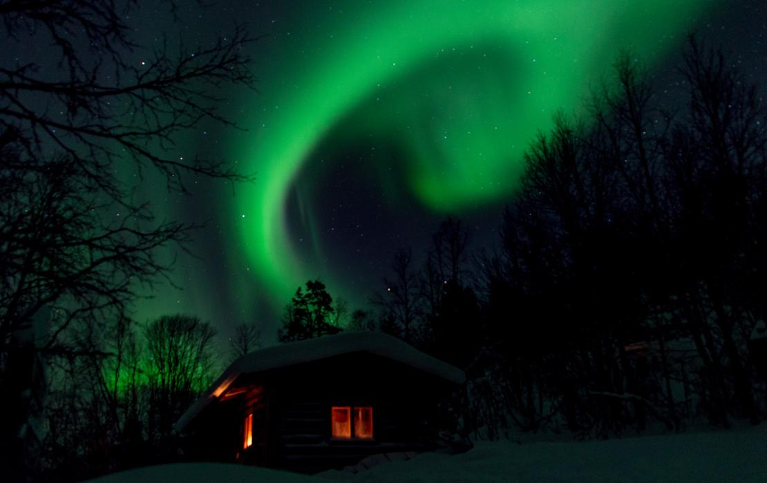 Northern lights dancing above a cabin in the Arctic night sky.