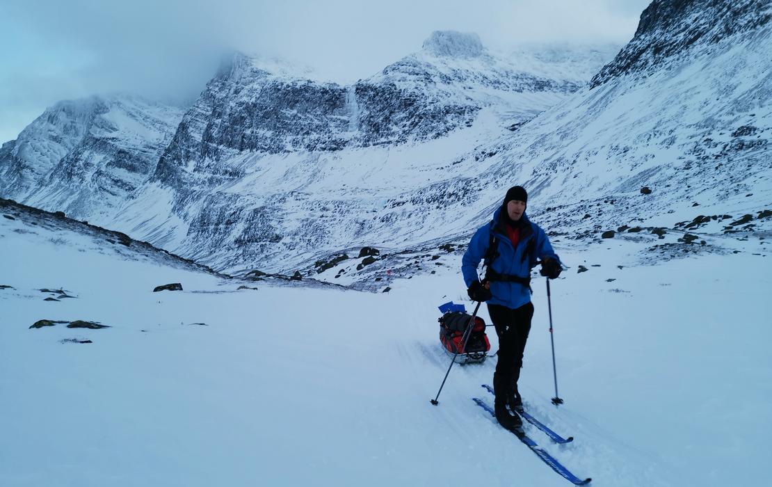 Solo skier pulling a sled through snowy Lapland mountains during an Arctic expedition.