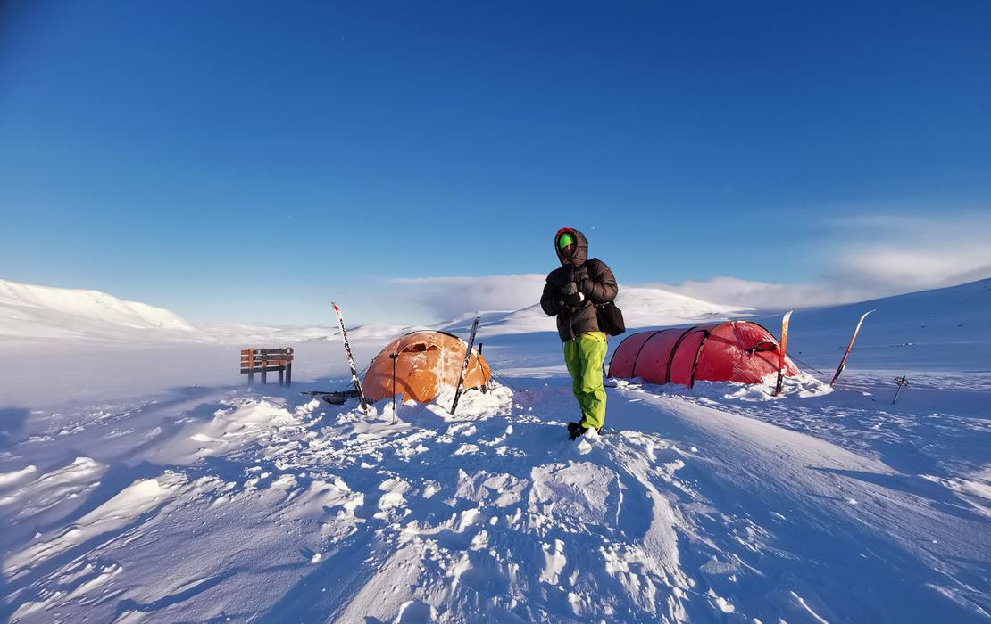 Person standing in Arctic mountain landscape in Lapland, with tents and skis in the snow.